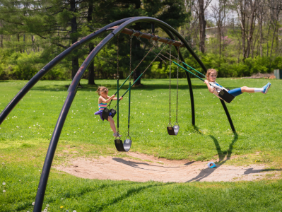 Two children swinging on a swing set in the park.